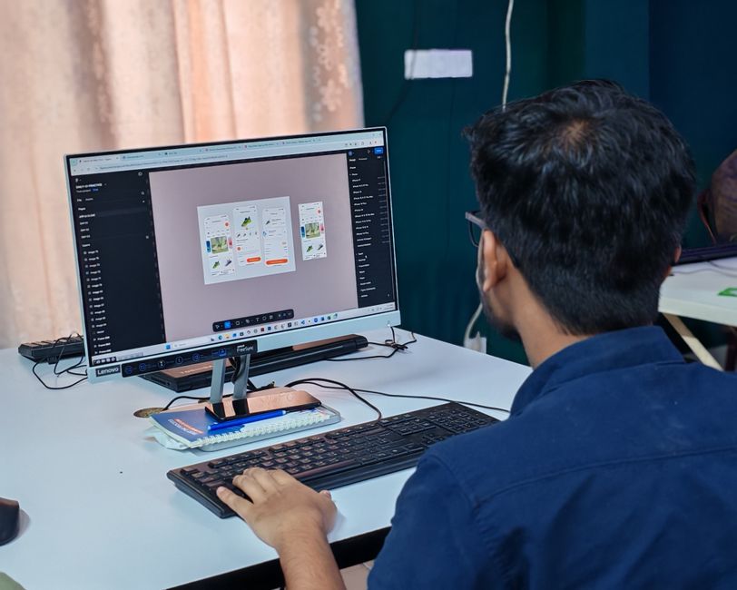 Un joven diseñador enfocado en crear interfaces de usuario en una computadora de escritorio en una oficina.